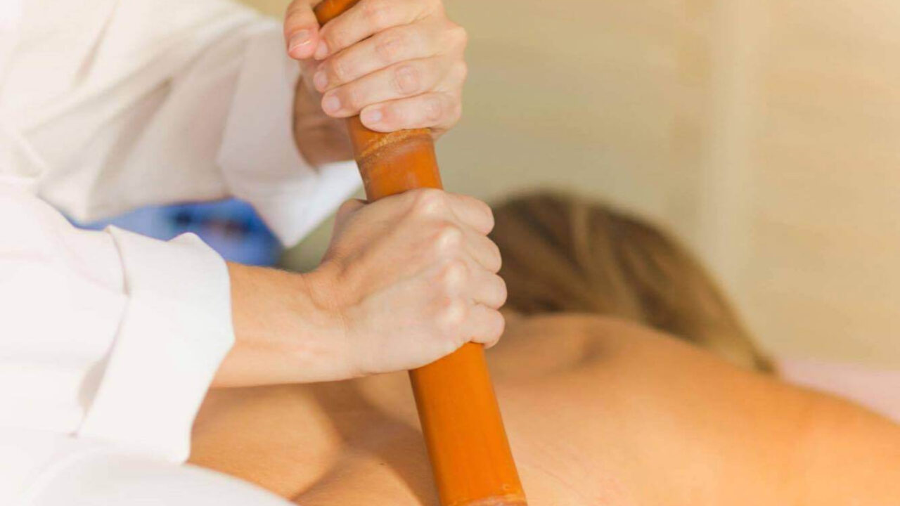 Terapeuta realizando uma massagem com bambu nas costas, promovendo relaxamento e alívio da tensão muscular.