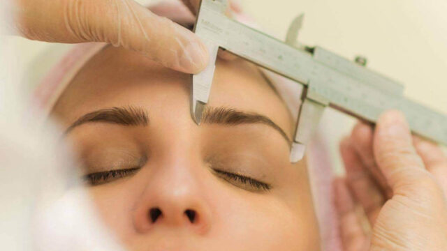 Procedimento de microblading fio a fio 3D sendo realizado, com a profissional medindo a simetria das sobrancelhas para um design perfeito e natural.